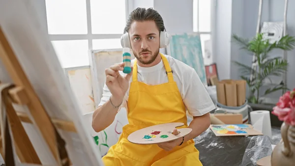 Young hispanic man artist having video call wearing headphones at art studio