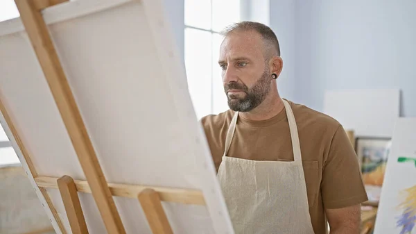 Handsome young man artist intensely drawing at his relaxed art studio, a creativity class bursting with paintbrushes, canvas and concentrated adult students.