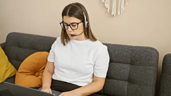 专注的女人 带着耳机 在舒适的客厅沙发上使用笔记本电脑 — 图库照片