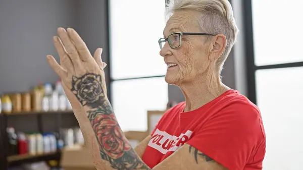 Confident grey-haired senior woman volunteer, radiating joy as she smiles and claps in applause at charity center, symbolizing altruistic community service