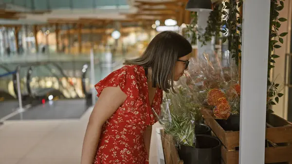メガネ付きの豪華なヒスパニック女性は 自信を持って立っている間に喜びを放射し 晴れた都市のショッピングセンターでカラフルな花を嗅ぎます — ストック写真