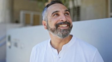 Gülümseyen yaşlı, gri sakallı, şehir caddesinde beyaz gömlekli bir adam.