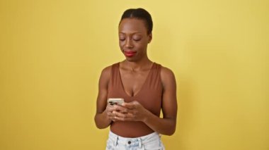 Neşeli Afro-Amerikalı kadın, sarı akıllı telefonuyla arka planda işaret edip gülümserken...