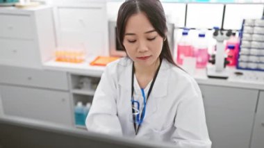 Beyaz laboratuvar önlüklü neşeli Çinli kadın bilim adamı dört numarayı parmaklarıyla gösteriyor, gülümsüyor ve laboratuvarı işaret ediyor. Eczane dünyasından olumlu bir sinyal.!