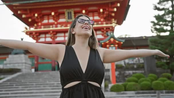 メガネに包まれたヒスパニック系女性は 京都で開かれた腕で自由を受け入れ 笑顔を浮かべ 大社を見回した — ストック動画