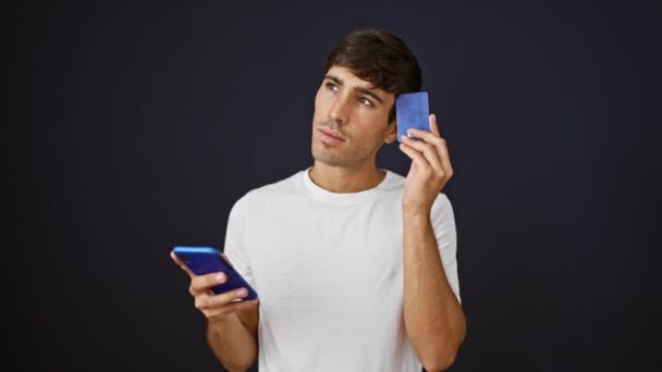 Młody Zamyślony Latynos Wątpiący Karty Kredytowe Telefon Odizolowanym Czarnym Tle — Wideo stockowe