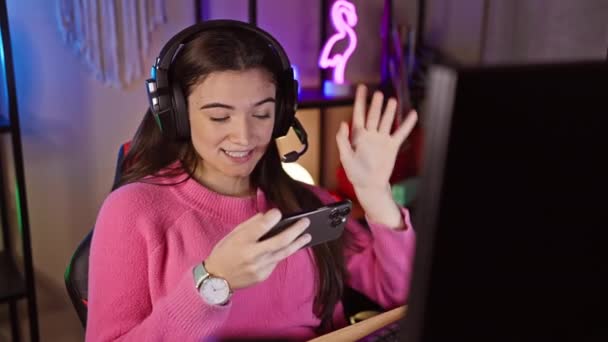 自宅のダークゲームルームでスマートフォンを使用してヘッドフォンを持つヒスパニック女性は 驚きと楽しみの感情を示しています — ストック動画