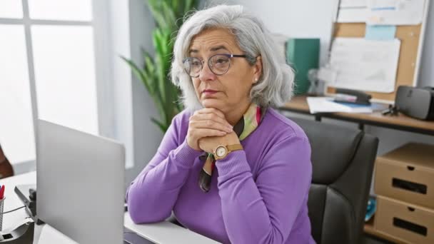 紫色のセーターの高齢女性は 彼女の現代のオフィスで休憩し 疲労や熟考を示しています — ストック動画