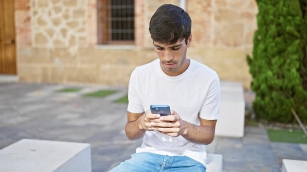 Νεαρός Ισπανός Που Χρησιμοποιεί Smartphone Σοβαρή Έκφραση Στο Πάρκο — Αρχείο Βίντεο