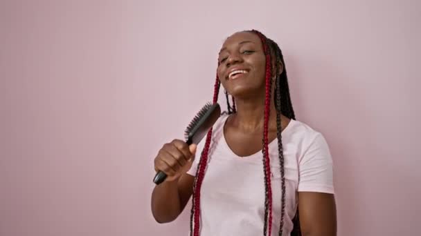 自信を持ったアフリカ系アメリカ人女性は マイクとしてブラシを使用して楽しく歌い 孤立したピンクの背景の上に踊ります — ストック動画