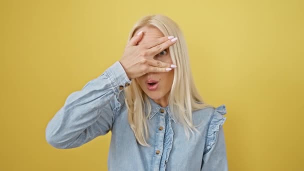 금발의 여자는 셔츠에 두려워하고 신속한 얼굴을 손가락을 놀라움에 노란색 배경에 — 비디오