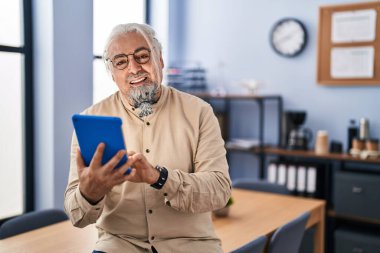 Orta yaşlı, gri saçlı iş adamı ofisteki dokunmatik pedi kullanarak gülümsüyor.