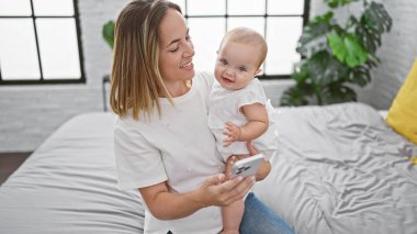 Sıcak yatak odasında, kendinden emin bir anne ve mutlu kızı birlikte biraz eğleniyorlar, yatakta oturmuş akıllı telefon ekranlarına bakıyorlar..
