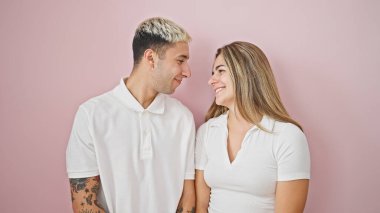 Güzel bir çift, pembe arka planda birbirlerine bakarak gülümsüyor.