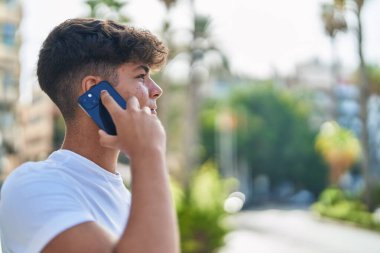Young hispanic teenager talking on smartphone with relaxed expression at street