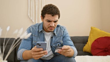 Akıllı telefon kullanan ve modern oturma odasında kredi kartı tutan odaklanmış bir adam..