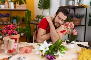 Çiçekçide çalışan genç İspanyol adam kendine sarılıyor mutlu ve pozitif, kendinden emin gülümsüyor. Sevgi ve özgüven. 