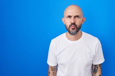 Mavi arka planda duran İspanyol dövmeli bir adam canlı yayında öpüşürken kameraya bakıyor. Sevimli ve seksi. aşk ifadesi. 