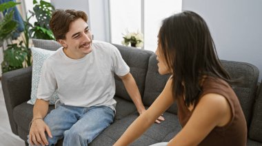 Bir erkek ve bir kadın modern evlerinde bir kanepeye yakın otururlar, keyifli bir anı paylaşırlar..