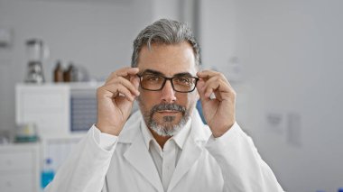 Yakışıklı, gri saçlı genç İspanyol bilim adamı canlı bir laboratuarda, çalışma masasında dururken mikroskopla analiz üzerine yoğunlaşarak ciddi şekilde tıbbi deneylere odaklanmış.