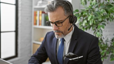 Çekici, gri saçlı, Latin kökenli, genç bir iş adamı. Kapalı alanda çalışmaya dalmış. Resepsiyonda çalışan işçiler, kulaklıkla ses dinleyerek dizüstü bilgisayara ciddi şekilde konsantre oluyorlar..