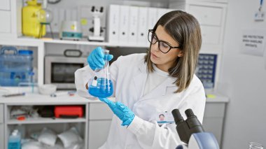 Profesyonel bir kadın bilim adamı, laboratuvar ortamında mavi bir sıvıyla deney tüpünü taşır. Konsantrasyon ve uzmanlık tasvir eder..