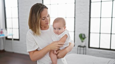 Rahat ve rahat, bir anne ayakta duruyor, sevgi dolu bir şekilde kızını kollarına alıyor, gerçek aşkını yumuşak bir öpücükle ifade ediyor..
