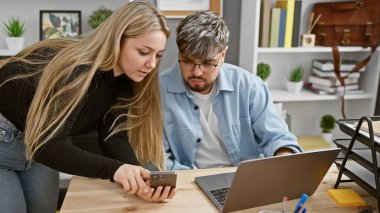 Modern bir ofis alanında akıllı telefondan iş birliği yapan bir erkek ve kadın, takım çalışması ve teknoloji çağrıştırıyor..