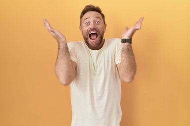 Sarı arka planda duran sakallı orta yaşlı adam çılgın ve başarıyı kollarını kaldırıp heyecanla haykırarak kutluyor. Kazanan konsept 