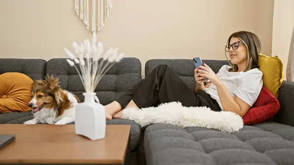 Młoda Kobieta Relaksuje Się Psem Kanapie Korzystając Smartfona Przytulnym Salonie — Zdjęcie stockowe