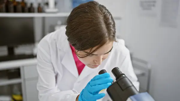 若いヒスパニック系女性科学者 美しいヘアスタイルを持ち 実験室で顕微鏡技術を用いた真剣な研究に魅了された — ストック写真