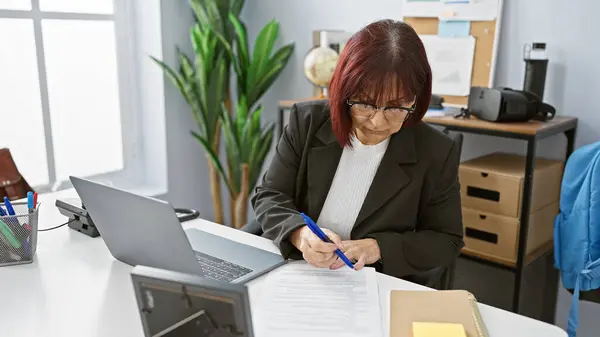 Hispanic Senior Woman Focused Signing Document Modern Office Workplace Setting — Stock Photo, Image