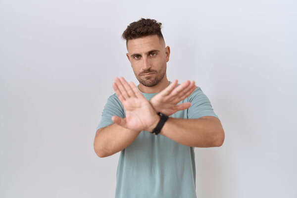 Hispanic man with beard standing over white background rejection expression crossing arms and palms doing negative sign, angry face 