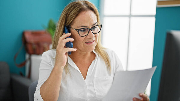 Middle age hispanic woman business worker talking on smartphone reading document at the office