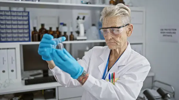 科学の中心では 研究所の試験管に集中した液体を測定する上級灰色の髪の女性科学者 — ストック写真