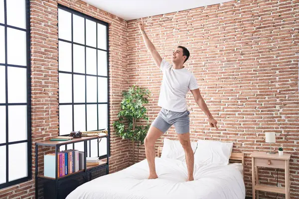 Young hispanic man smiling confident dancing on bed at bedroom