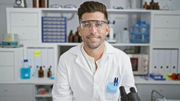 Confident young hispanic scientist with a handsome smile, working away in his indoor lab, a portrait of success as he puts safety first, wearing his security glasses and enjoying every test.