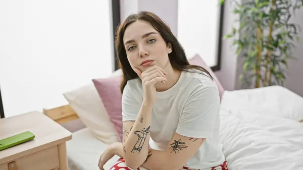 タトゥーのある熟考の若い女性が寝室に座り カジュアルな美しさと内省を発する — ストック写真
