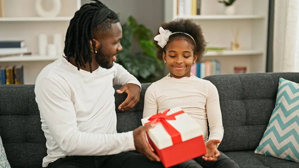 African american father and daughter surprise with gift sitting on sofa smiling at home