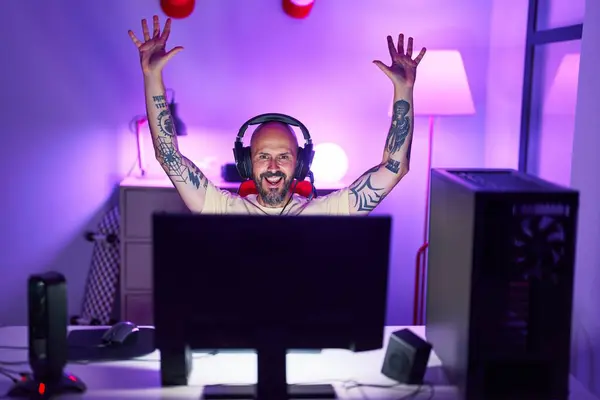 Young bald man streamer playing video game with winner expression at gaming room