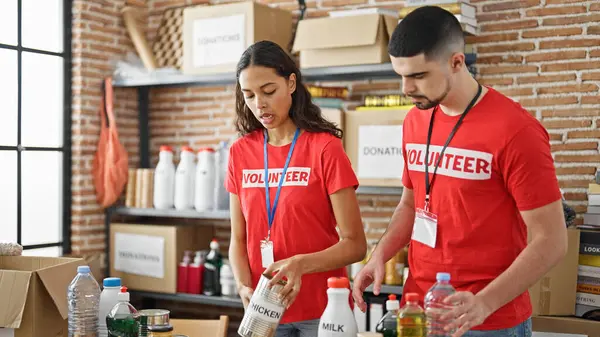 Man and woman volunteers, united in service, diligently checking box of donated products at the heart of charity center