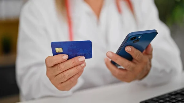 Middle age hispanic woman doctor shopping with smartphone and credit card at the clinic
