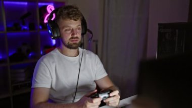 Odaklanmış, sakallı ve mavi gözlü beyaz adam geceleri karanlık bir oyun odasında oyun oynuyor.