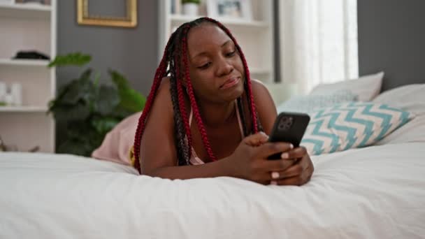 寝室のベッドで携帯電話を使用してパジャマで驚いたアフリカ系アメリカ人女性 — ストック動画