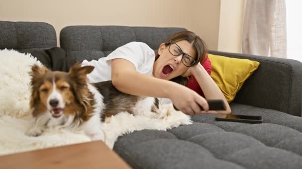 Young Hispanic Woman Yawns While Lying Couch Her Dog Remote — Stock Video