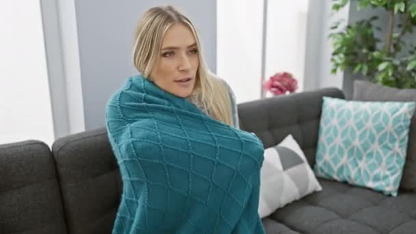 美しい若いブロンドの女性 彼女のアパートの居心地の良い暖かさで凍結 ソファの上に座って インフルエンザの寒い熱と戦う毛布にスワッド — ストック動画