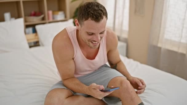 在明亮的卧室里躺在床上时 一个头戴水槽盖的快乐男人用智能手机 — 图库视频影像