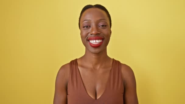 陽気で自信を持って見える陽気なアフリカ系アメリカ人女性は 黄色の背景に隔離された歯痛のある笑顔で喜びを放射します — ストック動画