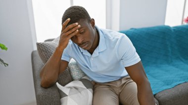 Düşünceli bir Afro-Amerikan erkeği evde oturur, bir ev ortamında endişe veya tefekkür tasvir eder..