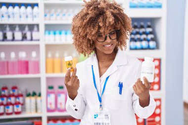 African american woman pharmacist smiling confident holding pills bottles at pharmacy